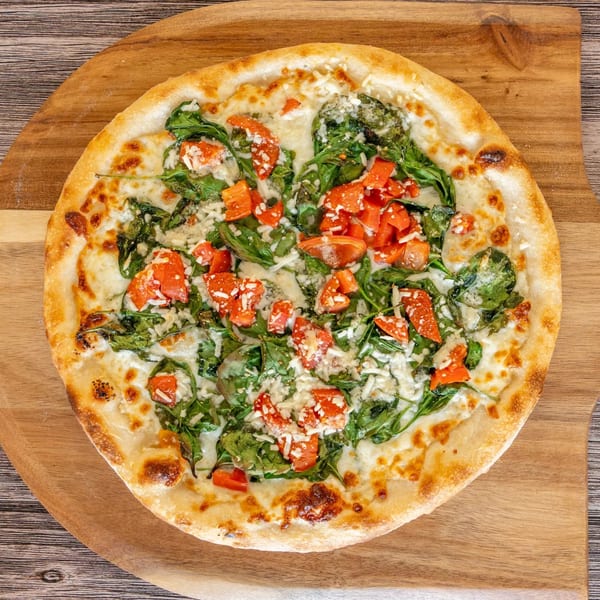 Bryan Place Pizza & Pasta's NY-style white pizza with spinach, diced tomatoes, and cheese on a wooden peel.