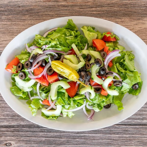 Fresh garden salad with lettuce, tomatoes, cucumbers, red onions, black olives, and a pepperoncini.