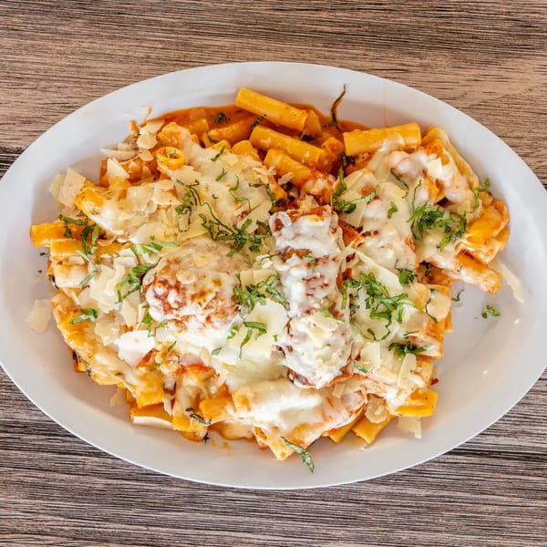 Baked ziti pasta with melted mozzarella, parmesan, and fresh basil on a white plate.