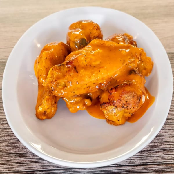 A white plate holds several Bryan Place Pizza & Pasta chicken wings coated in a vibrant orange sauce.