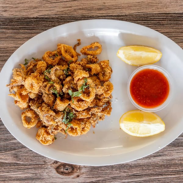 Crispy fried calamari with fresh parsley, lemon wedges, and a side of marinara sauce on a white plate.