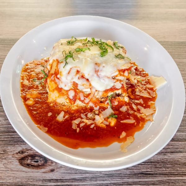 A generous serving of lasagna with melted cheese, tomato sauce, and fresh basil on a white plate.